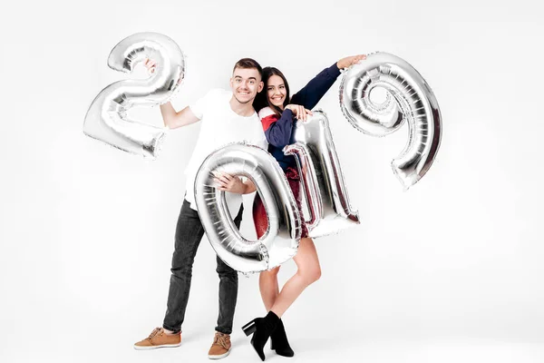 Смішна дівчина і хлопець, одягнені в стильний розумний одяг, тримають повітряні кулі у формі цифр 2019 року на білому тлі в студії — стокове фото