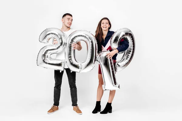 Χαμογελαστό κορίτσι και άντρας ντυμένος με ένα κομψό ρούχα τη διασκέδαση με μπαλόνια με τη μορφή των αριθμών 2019 σε λευκό φόντο στο στούντιο — Φωτογραφία Αρχείου
