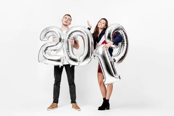 Усміхнена дівчина і хлопець, одягнені в стильний одяг, розважаються з повітряними кулями у формі цифр 2019 року на білому тлі в студії — стокове фото