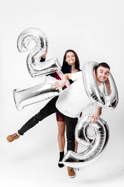 Κοπέλα και άντρας ντυμένος με ένα κομψό έξυπνο ρούχα τη διασκέδαση με μπαλόνια με τη μορφή των αριθμών 2019 σε λευκό φόντο στο στούντιο — Φωτογραφία Αρχείου