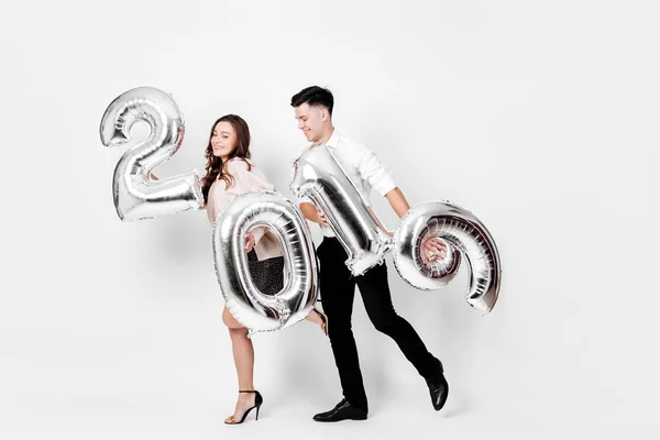 Chica feliz y chico vestido con una ropa elegante con estilo están sosteniendo globos en forma de números 2019 sobre un fondo blanco en el estudio — Foto de Stock