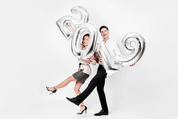 Menina engraçada e cara vestida com uma roupa elegante inteligente estão segurando balões na forma de números 2019 em um fundo branco no estúdio — Fotografia de Stock