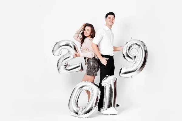 Girl and guy dressed in a stylish smart clothes are holding ballon in the shape of numbers 2019 on a white background in the studio — Stok Foto