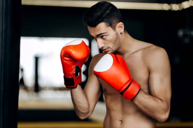Sporcu çıplak bir gövde ve ellerinin üstünde kırmızı boks eldiven boks jimnastik salonu tetikte duruyor