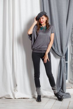 Moda kız stüdyoda pozlar yeşil boncuk, gri kot pantolon ve şık bir kap ile şık bir gri bluz giymiş