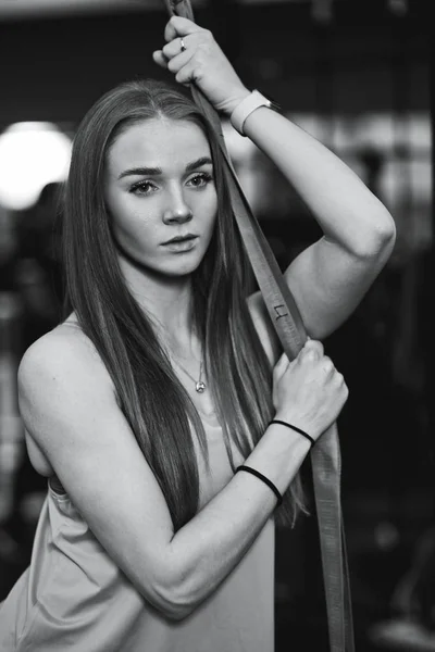 Чорно-біле фото красивої спортивної дівчини, одягненої у спортивний одяг, що стоїть у спортзалі поруч зі спортивним обладнанням — стокове фото