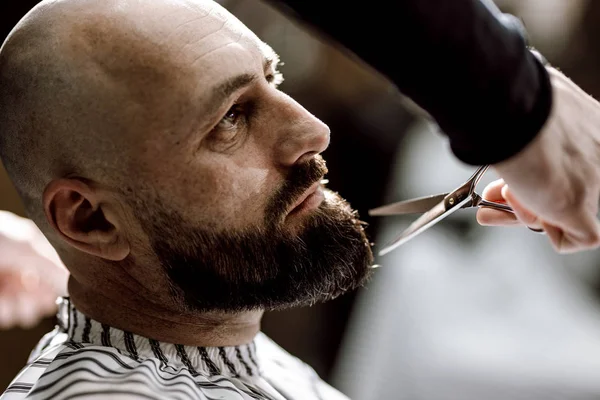 Парикмахер моды одет в черную одежду ножницы бороду жестокого человека в стильной парикмахерской — стоковое фото
