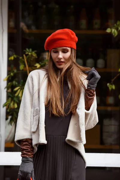 Модная девушка, одетая в стильное серое платье, короткое пальто из овчины, перчатки и красные береты прогулки в парке в солнечный день — стоковое фото