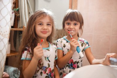 İki küçük güzel kız kardeş aynı gömlek fırça onların dişler banyoda giyinmiş