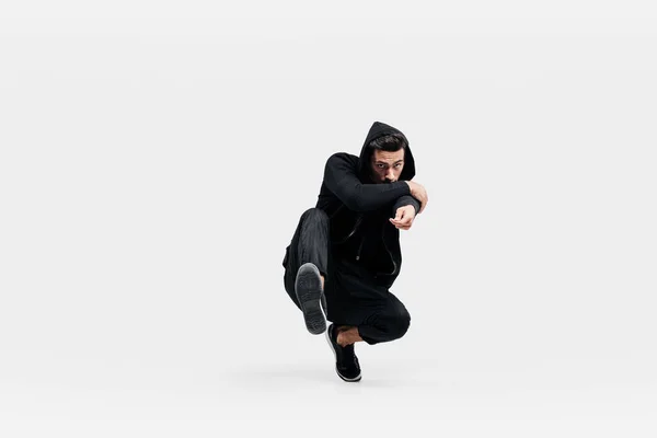 Przystojny młody tancerz na sobie czarne spodnie i czarną bluzę tańczy breakdance robi taniec ruchy na podłodze — Zdjęcie stockowe