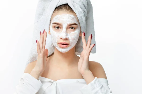 Menina agradável em uma roupa branca com uma toalha branca em seu cabelo coloca uma máscara cosmética em seu rosto — Fotografia de Stock