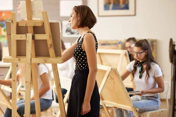 Professor de desenho encantador no vestido bonito mostra técnica de desenho no cavalete no estúdio de arte — Fotografia de Stock