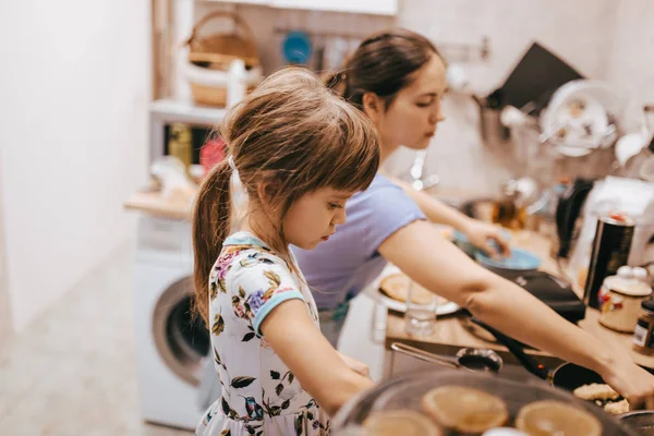 Mãe e sua filha cozinhar panquecas para o café da manhã na pequena cozinha aconchegante — Fotografia de Stock