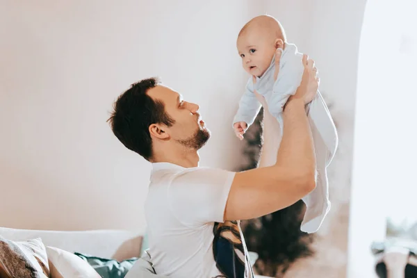 Mladý otec drží své malé slunce na pohovce v místnosti se světlem — Stock fotografie