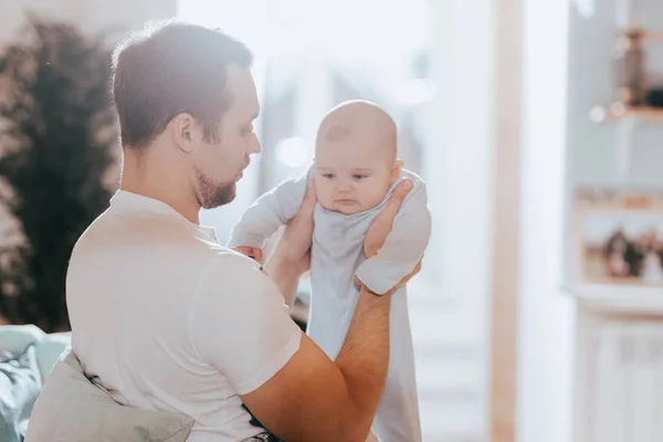 Junger Vater hält seine winzige Sonne auf dem Sofa im hellen Zimmer in den Armen — Stockfoto