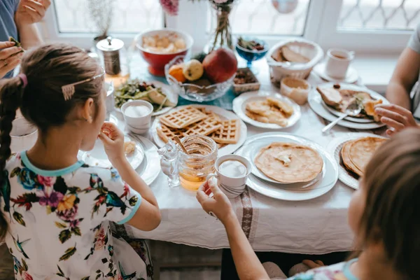 Familienfrühstück zu Hause in der gemütlichen Küche. Mutter, Vater und ihre beiden Töchter essen Pfannkuchen — Stockfoto