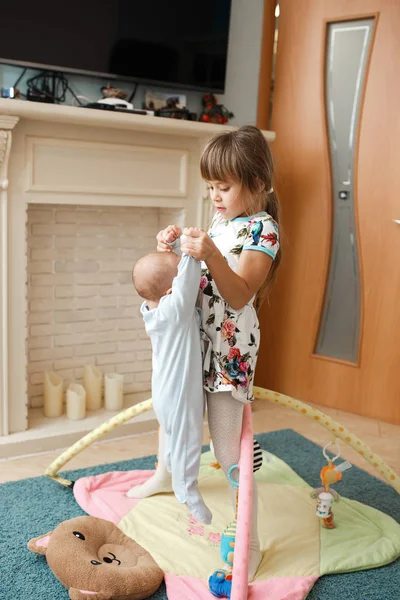 Μικρό γοητευτικό κορίτσι κρατά τον μικρό αδελφό για το χαλί στο πάτωμα στο δωμάτιο — Φωτογραφία Αρχείου