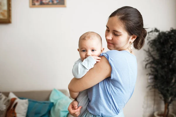 Junge Mutter in hellblauem T-Shirt und Rock hält ihren winzigen Sohn auf dem Arm im heimischen Zimmer — Stockfoto