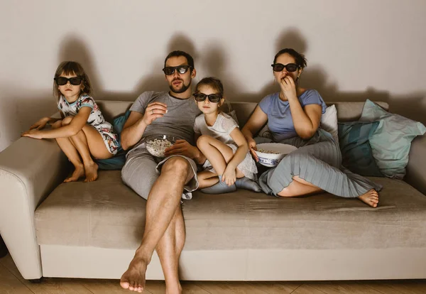 Ευτυχισμένη οικογένεια ο πατέρας, μητέρα και δύο κόρες με τα ειδικά γυαλιά, βλέποντας τηλεόραση και τρώγοντας ποπ κορν που κάθεται στον καναπέ — Φωτογραφία Αρχείου