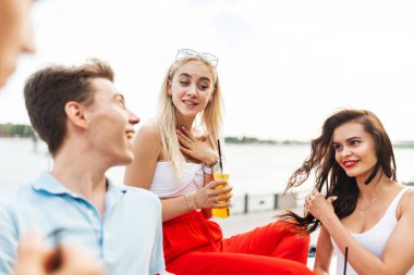 Gülüyor ve sarı kokteyl içme ve Nehri yanındaki güzel kafede sosyalleşme yakışıklı arkadaş şirket. Şerefe. Eğlence, iyi vakit geçiriyor. Arka planda nehirdir.