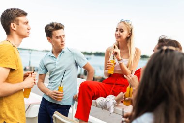 Gülüyor ve Nehri yanındaki güzel kafede sarı kokteyl içme yakışıklı arkadaş şirket. Şerefe. Eğlence, iyi vakit geçiriyor. Arka planda nehirdir.