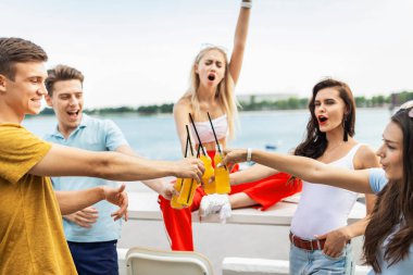 Gülüyor ve Nehri yanındaki güzel kafede sarı kokteyl içme yakışıklı arkadaş şirket. Şerefe. Eğlence, iyi vakit geçiriyor. Arka planda nehirdir.