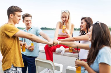 Gülüyor ve sarı kokteyl içme ve Nehri yanındaki güzel kafede sosyalleşme yakışıklı arkadaş şirket. Şerefe. Eğlence, iyi vakit geçiriyor. Arka planda nehirdir.