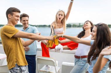 Gülüyor ve Nehri yanındaki güzel kafede sarı kokteyl içme yakışıklı arkadaş şirket. Şerefe. Eğlence, iyi vakit geçiriyor. Arka planda nehirdir.