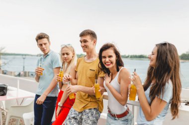 Gülüyor ve Nehri yanındaki güzel kafede sarı kokteyl içme yakışıklı arkadaş şirket. Şerefe. Eğlence, iyi vakit geçiriyor. Arka planda nehirdir.