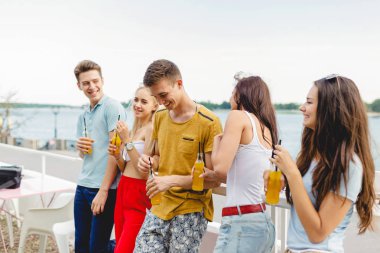 Gülüyor ve Nehri yanındaki güzel kafede sarı kokteyl içme yakışıklı arkadaş şirket. Şerefe. Eğlence, iyi vakit geçiriyor. Arka planda nehirdir.