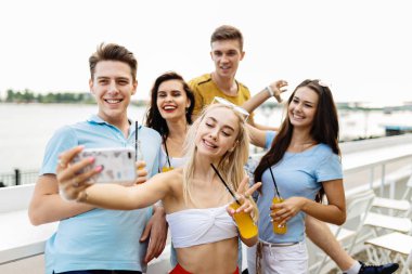 Gülüyor ve sarı kokteyl içme ve sosyalleşme ve selfie Nehri yanındaki güzel kafede yapma yakışıklı arkadaş şirket. Şerefe. Eğlence, iyi vakit geçiriyor. Nehir olduğunu