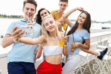 Gülüyor ve sarı kokteyl içme ve sosyalleşme ve selfie Nehri yanındaki güzel kafede yapma yakışıklı arkadaş şirket. Şerefe. Eğlence, iyi vakit geçiriyor. Nehir olduğunu