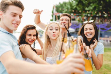 Gülüyor ve sarı kokteyl içme ve Nehri yanındaki güzel kafede sosyalleşme yakışıklı arkadaş şirket. Şerefe. Eğlence, iyi vakit geçiriyor. Arka planda nehirdir.