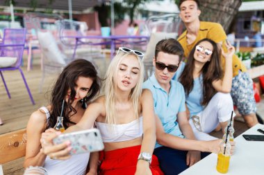 Sosyalleşme ve güzel yaz kafede masada selfie yapma gülüyor ve sarı kokteyller, içme yakışıklı arkadaş şirket. Şerefe. Eğlence, iyi vakit geçiriyor. Dostluk.