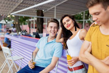 Gülüyor, sarı kokteyl içme ve güzel yaz kafe barda sosyalleşme yakışıklı arkadaş şirket. Şerefe. Eğlence, iyi vakit geçiriyor. Dostluk.