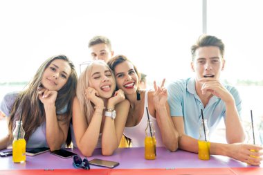 Gülüyor, sarı kokteyl içme ve güzel yaz kafe barda sosyalleşme yakışıklı arkadaş şirket. Arka planda nehirdir. Şerefe. Eğlence, iyi vakit geçiriyor