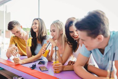 Gülüyor, sarı kokteyl içme ve güzel yaz kafe barda sosyalleşme yakışıklı arkadaş şirket. Arka planda nehirdir. Şerefe. Eğlence, iyi vakit geçiriyor