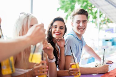 Gülüyor, sarı kokteyl içme ve güzel yaz kafe barda sosyalleşme yakışıklı arkadaş şirket. Arka planda nehirdir. Şerefe. Eğlence, iyi vakit geçiriyor