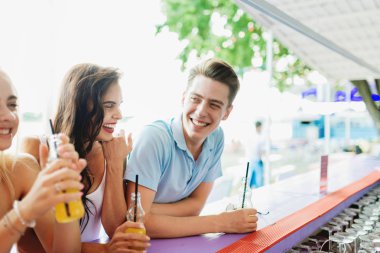 Gülüyor, sarı kokteyl içme ve güzel yaz kafe barda sosyalleşme yakışıklı arkadaş şirket. Arka planda nehirdir. Şerefe. Eğlence, iyi vakit geçiriyor