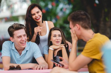 Yakışıklı arkadaş bir şirket gülüyor, sosyalleşme ve güzel yaz kafede masada oturuyor. Eğlence, iyi vakit geçiriyor. Dostluk.