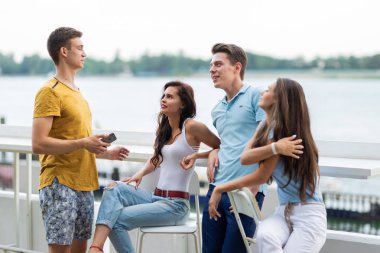 Yakışıklı arkadaş bir şirket gülüyor ve güzel yaz kafede sohbet. Arka planda nehirdir. Eğlence, iyi vakit geçiriyor. Dostluk.