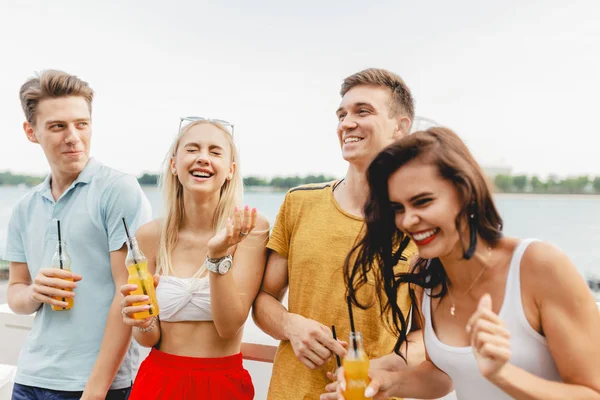 A company of good-looking friends laughing and drinking yellow cocktails in the nice cafe next to the river. Cheers. Entertainment, having good time. River is in the background.