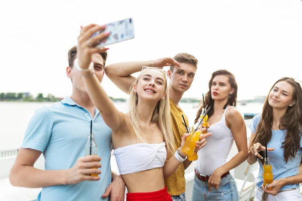 Gülüyor ve sarı kokteyl içme ve sosyalleşme ve selfie Nehri yanındaki güzel kafede yapma yakışıklı arkadaş şirket. Şerefe. Eğlence, iyi vakit geçiriyor. Nehir olduğunu