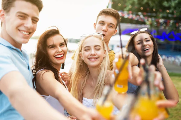 A company of good-looking friends laughing and drinking yellow cocktails and socialising  in the nice cafe next to the river. Cheers. Entertainment, having good time. River is in the background.