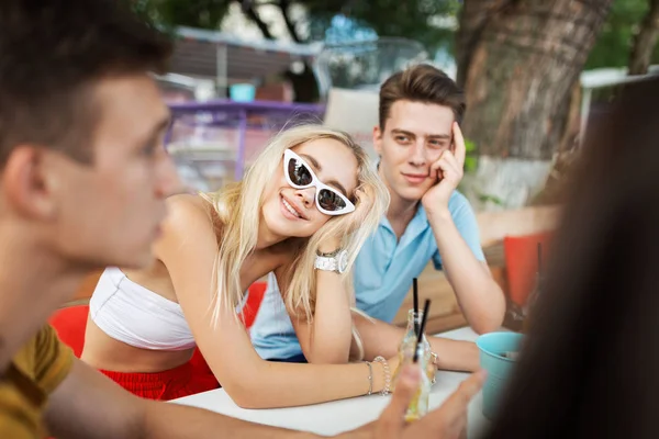 Eine Gesellschaft gut aussehender Freunde, die lachen und gelbe Cocktails trinken und sich am Tisch im netten Sommercafé treffen. Jubel. Unterhaltung, Spaß haben. Freundschaft. — Stockfoto