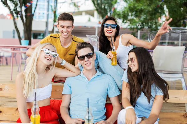 一个帅气的朋友们戴着太阳镜, 在美丽的夏季咖啡馆里笑着喝着黄色的鸡尾酒, 在餐桌上社交。干杯。娱乐, 有很好的时间。友谊. — 图库照片