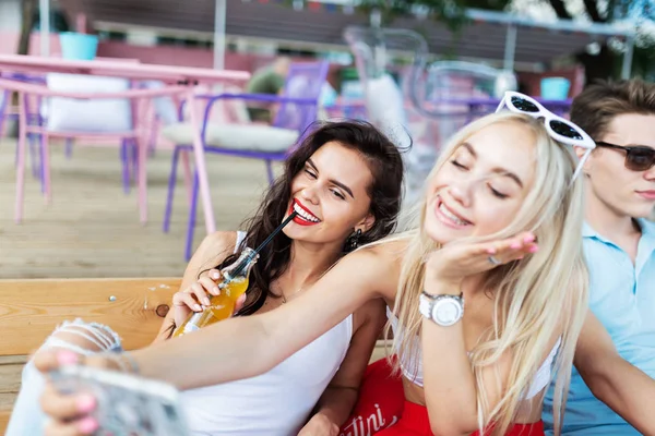 Una compañía de amigos guapos que ríen y beben cócteles amarillos, socializando y haciendo selfies en la mesa de la bonita cafetería de verano. ¡Salud! Entretenimiento, pasándolo bien. Amistad . — Foto de Stock