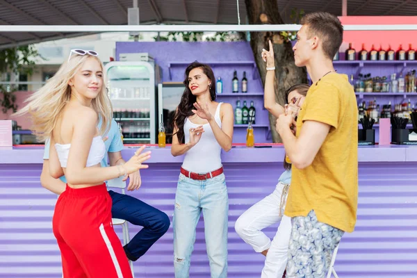 Una compañía de amigos guapos riendo, bebiendo cócteles amarillos, bailando y socializando en el bar en el agradable café de verano. ¡Salud! Entretenimiento, pasándolo bien. Amistad . —  Fotos de Stock