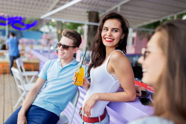 A company of good-looking friends laughing, drinking yellow cocktails and socialising at the bar in the nice summer cafe. Cheers. Entertainment, having good time. Friendship.