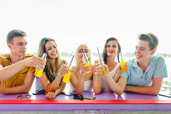 一个由帅哥朋友组成的公司在一家漂亮的夏季咖啡馆的酒吧里大笑, 喝着黄色的鸡尾酒, 并在酒吧里社交。河在背景中。干杯。娱乐, 有好时机 — 图库照片